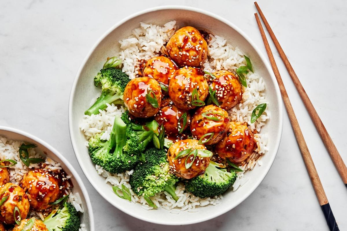 a bowl of homemade teriyaki meatballs served on top of white rice with steamed broccoli