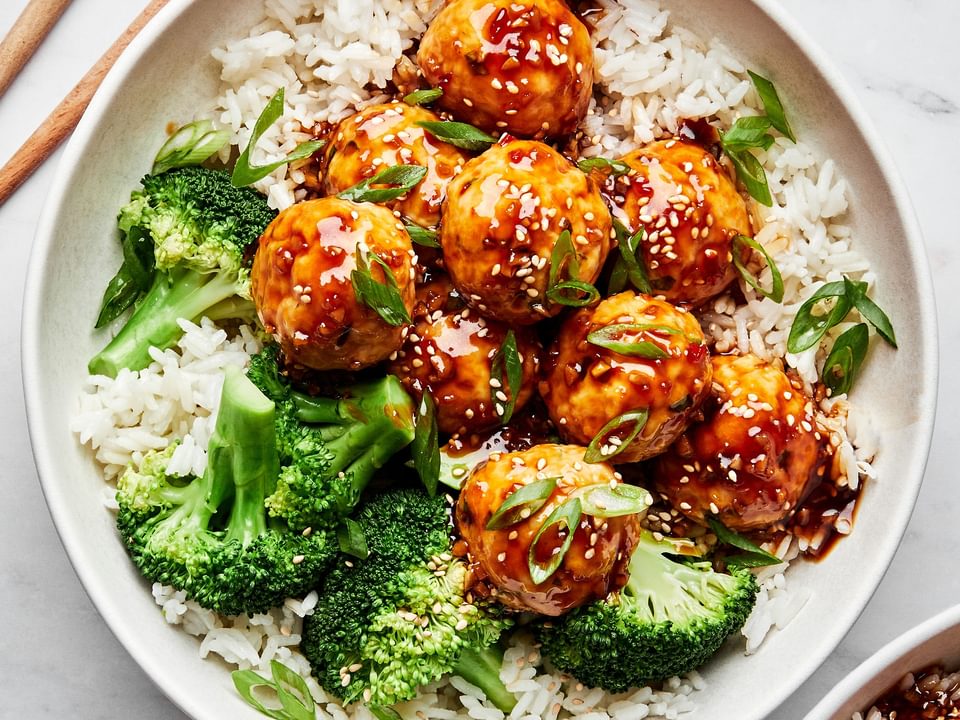 homemade teriyaki meatballs served over white rice with steamed broccoli next to chopsticks