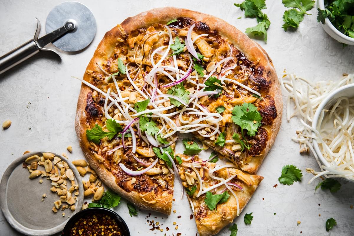 Thai style chicken pizza with cheese. onions, hoisin sauce and peanuts with a slice out of it
