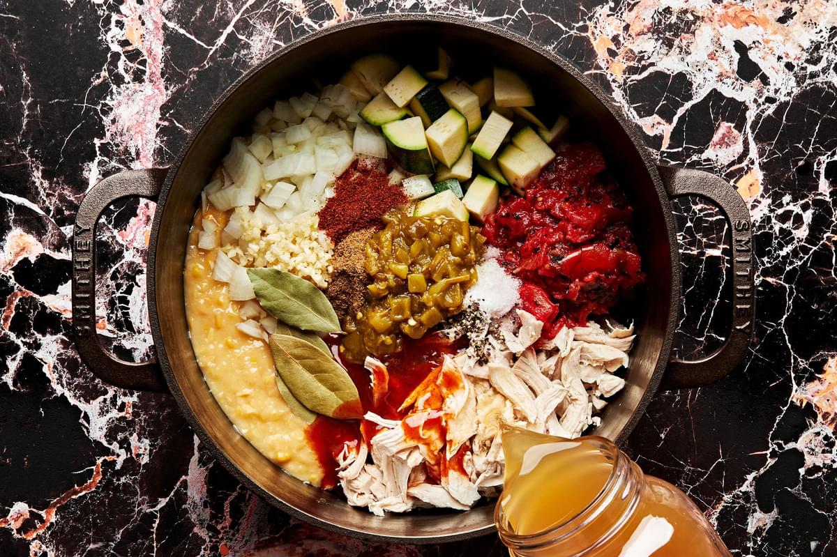 chicken, stock, enchilada sauce, creamed corn, diced tomatoes, onion, zucchini, chiles and spices being combined in a pot