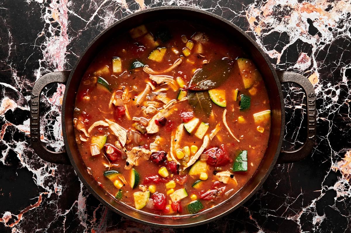 a pot of chicken tortilla soup made with enchilada sauce, creamed corn, diced tomatoes, onion, zucchini, chiles and spices