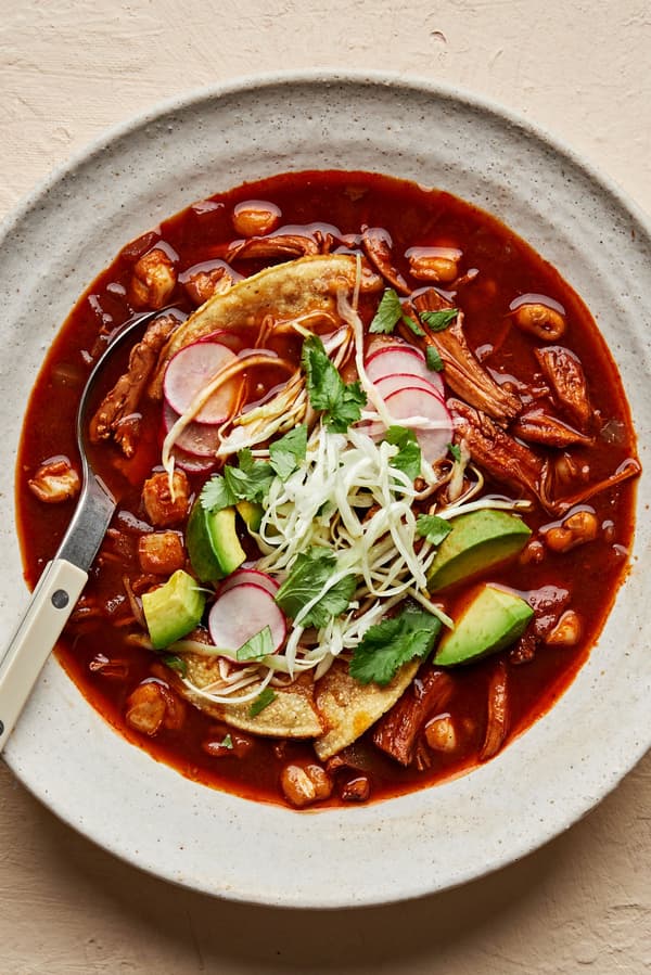 a bowl of homemade turkey pozole rojo topped with seasoned cabbage, avocado, cilantro, radishes, and lime juice.