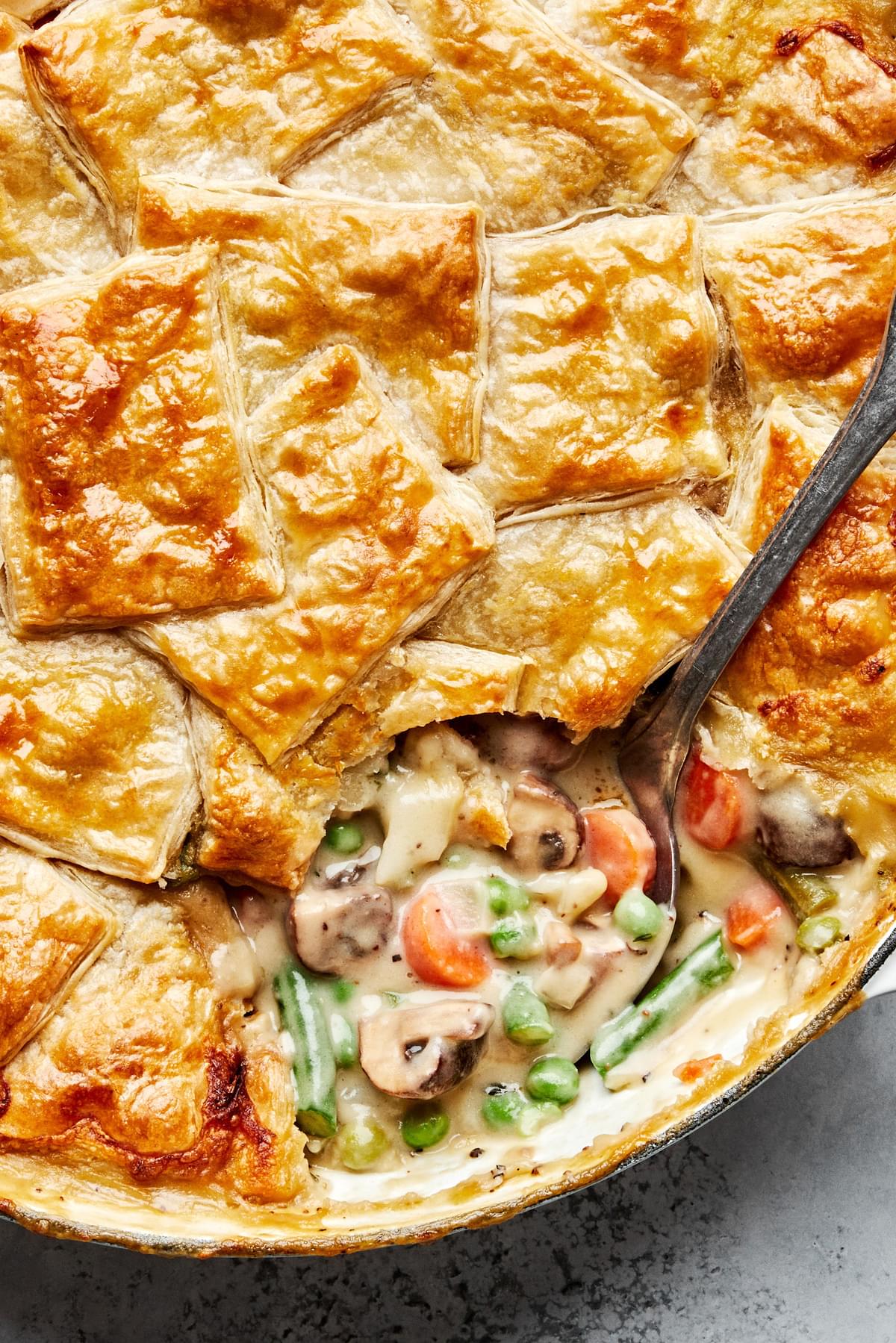 a homemade vegetable pot pie in a skillet made with green beans, peas and mushrooms being scooped into a bowl