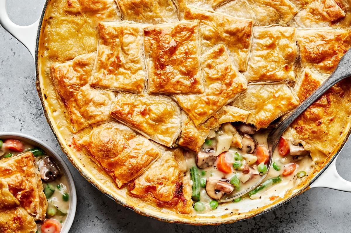 a homemade vegetable pot pie in a skillet made with green beans, peas and mushrooms being scooped into a bowl