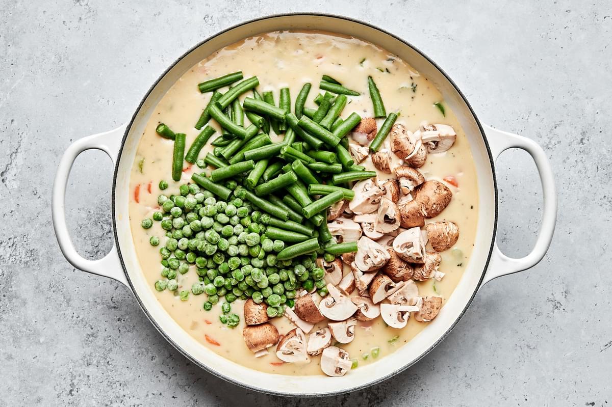 green beans, peas and mushrooms being added to a skillet with vegetable pot pie filling