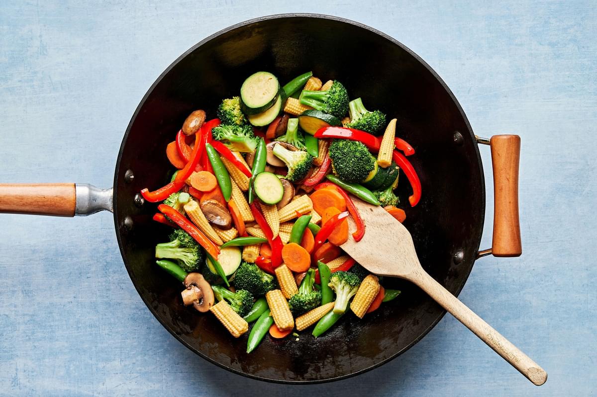 mushrooms, broccoli, corn, pepper, snap peas, zucchini & carrots being cooked in vegetable oil in a wok