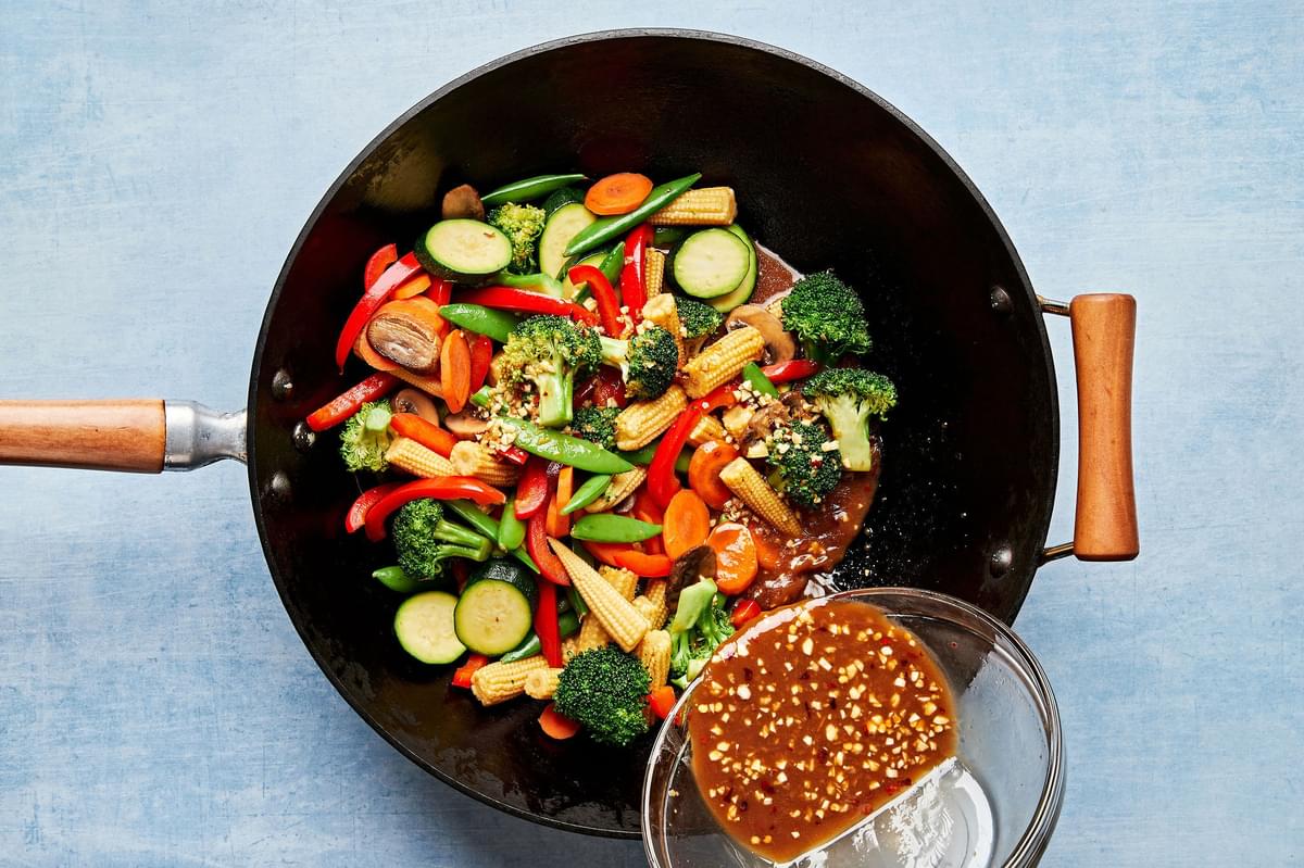 homemade sauce being poured on top of stir fry vegetables in a wok