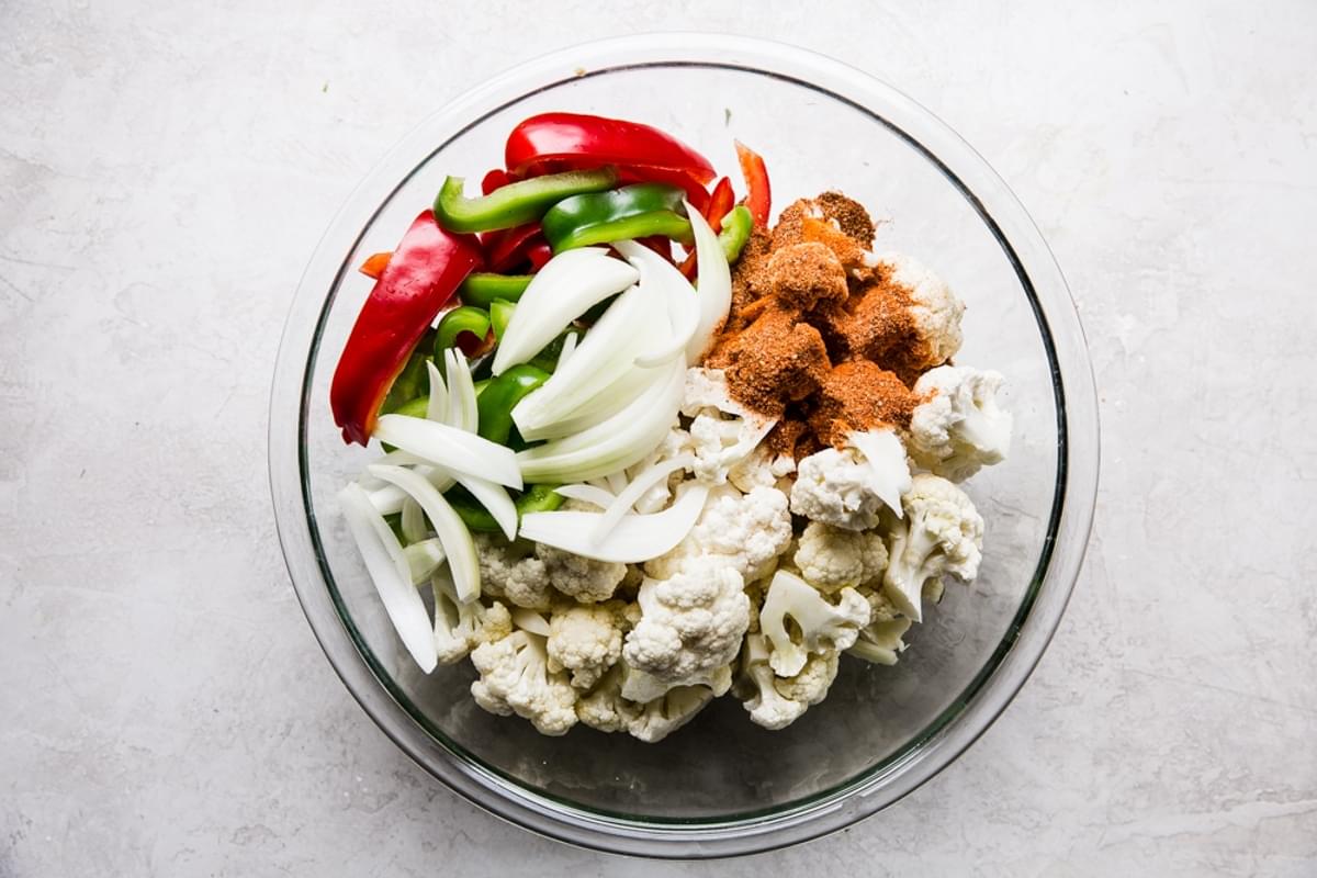 cauliflower, red and green bell peppers, onion and taco seasoning in a glass mixing bowl
