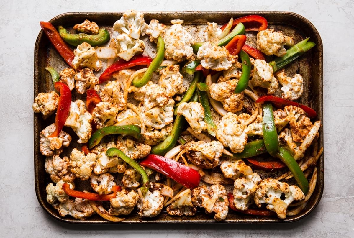 cauliflower, red and green bell peppers on a baking sheet with taco seasoning, olive oil and lime juice