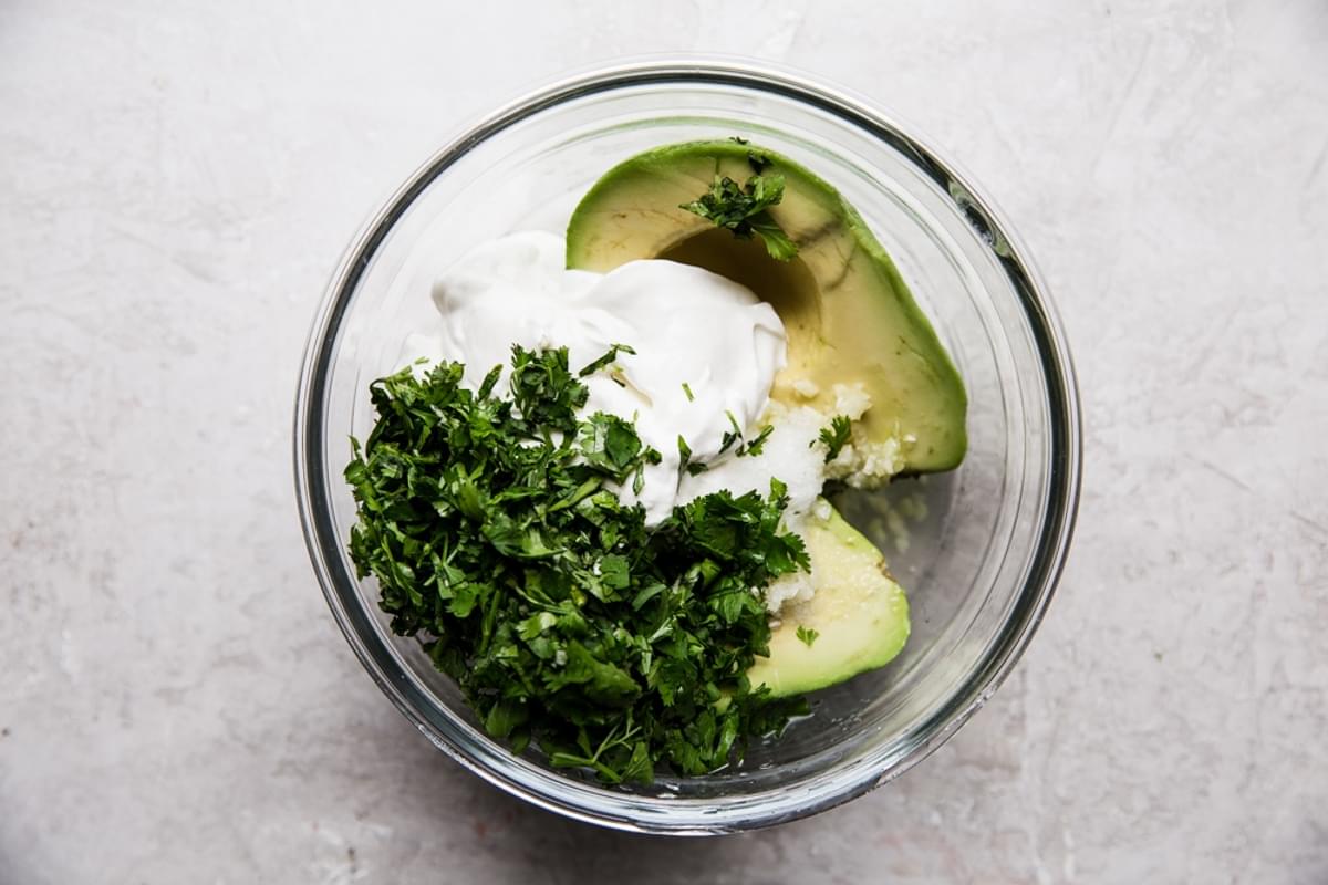 Avocado, cilantro, sour cream and lime juice in a small glass mixing bowl