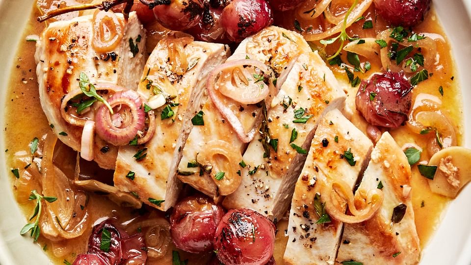 oven baked chicken breast sliced in a serving bowl with cooked  shallots, parsley and red grapes
