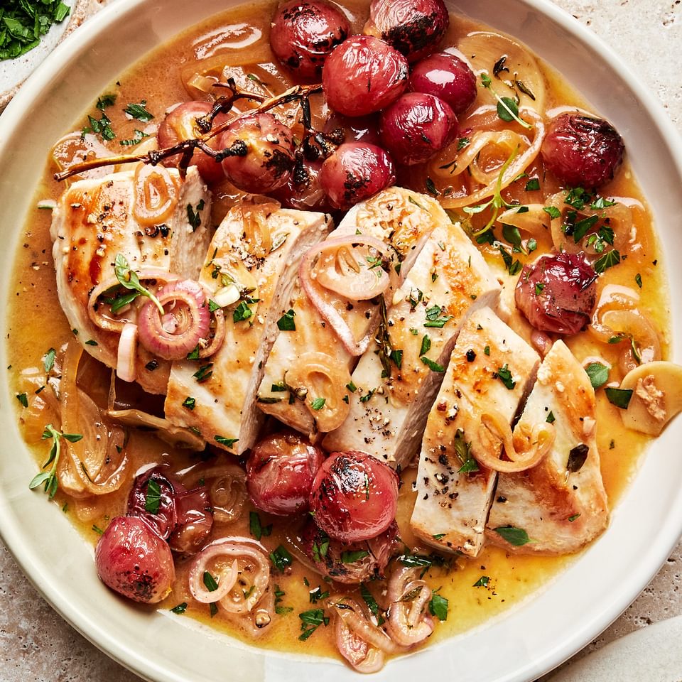 oven baked chicken breast sliced in a serving bowl with cooked  shallots, parsley and red grapes