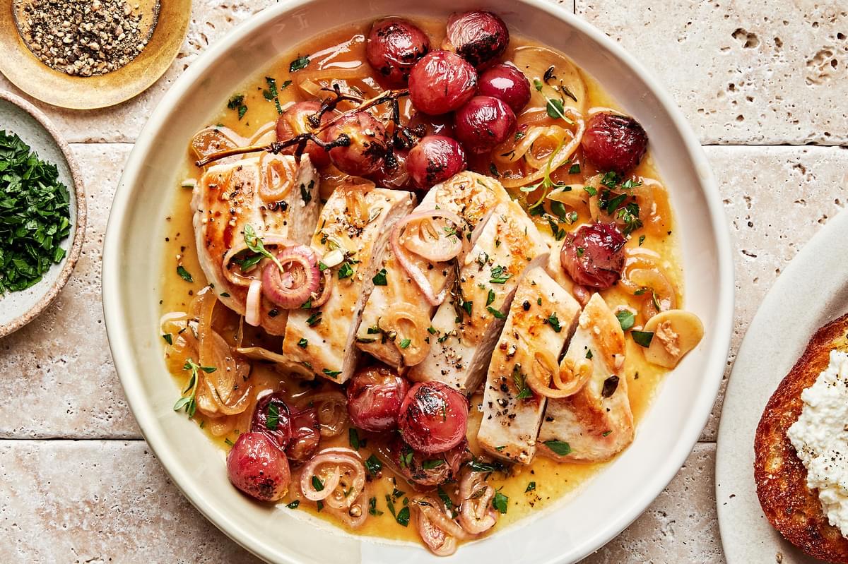 vineyard chicken sliced in a serving bowl with cooked shallots, parsley and red grapes