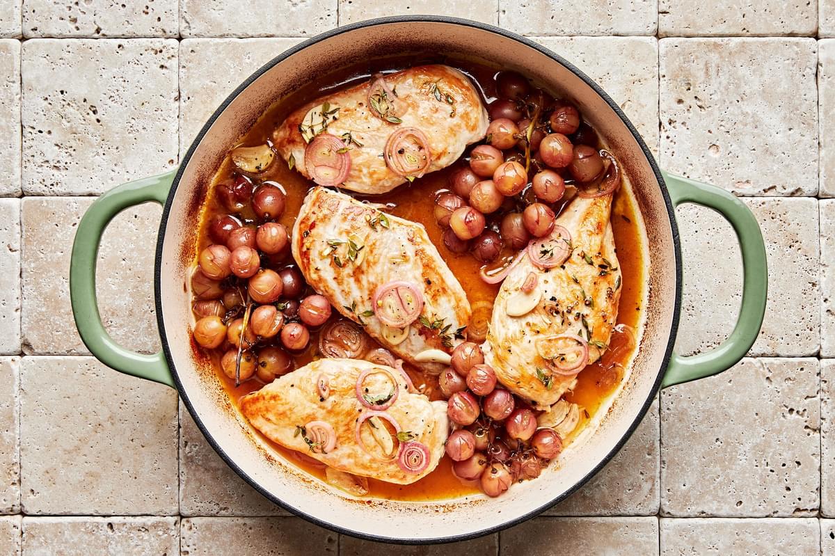 vineyard chicken cooking in a skillet with shallots, garlic and red grapes