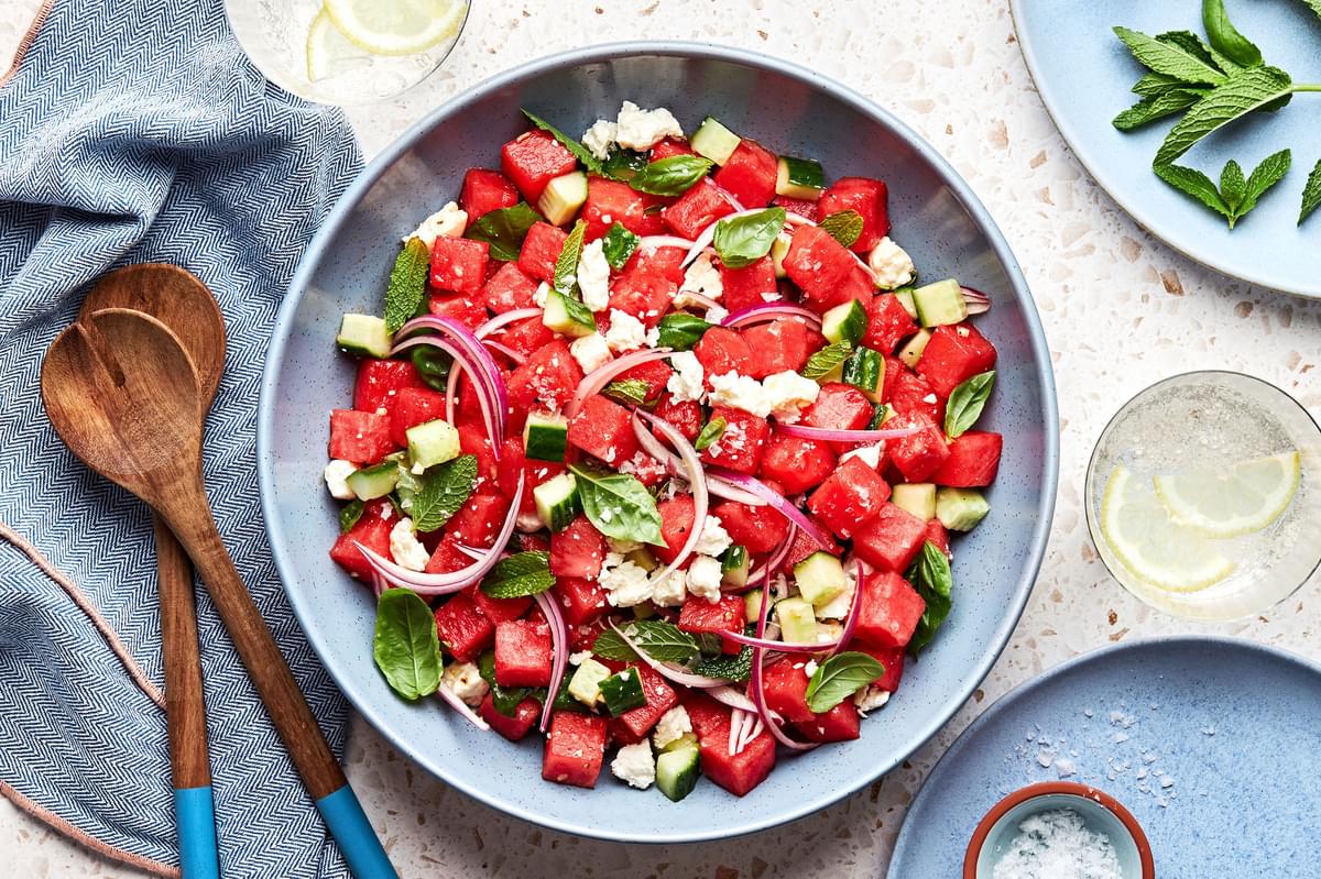 watermelon salad in a bowl made with, cucumber, red onion, feta, mint and basil with a white balsamic dressing