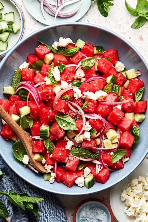 watermelon salad in a serving bowl made with, cucumber, red onion, feta, mint and basil with a balsamic dressing