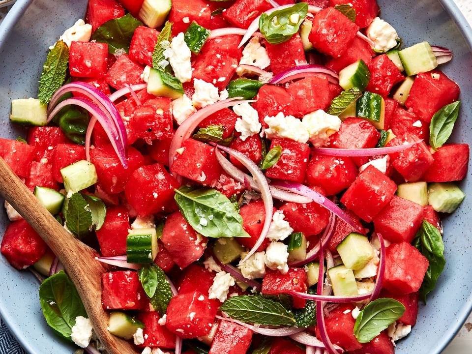 watermelon salad in a serving bowl made with, cucumber, red onion, feta, mint and basil with a balsamic dressing
