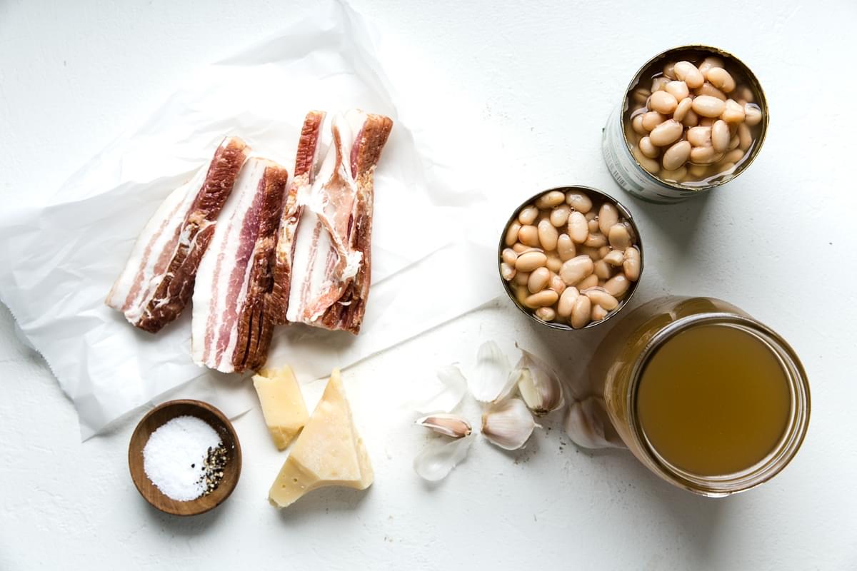 Ingredients laid out for white bean soup with bacon, broth, parmesan cheese, garlic and salt