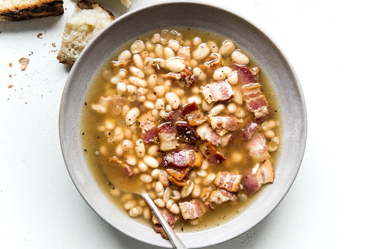 white bean and bacon soup in a bowl with a spoon garlic and chicken stock