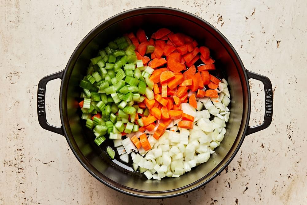 onion, celery and carrots being cooked in olive oil in a large pot