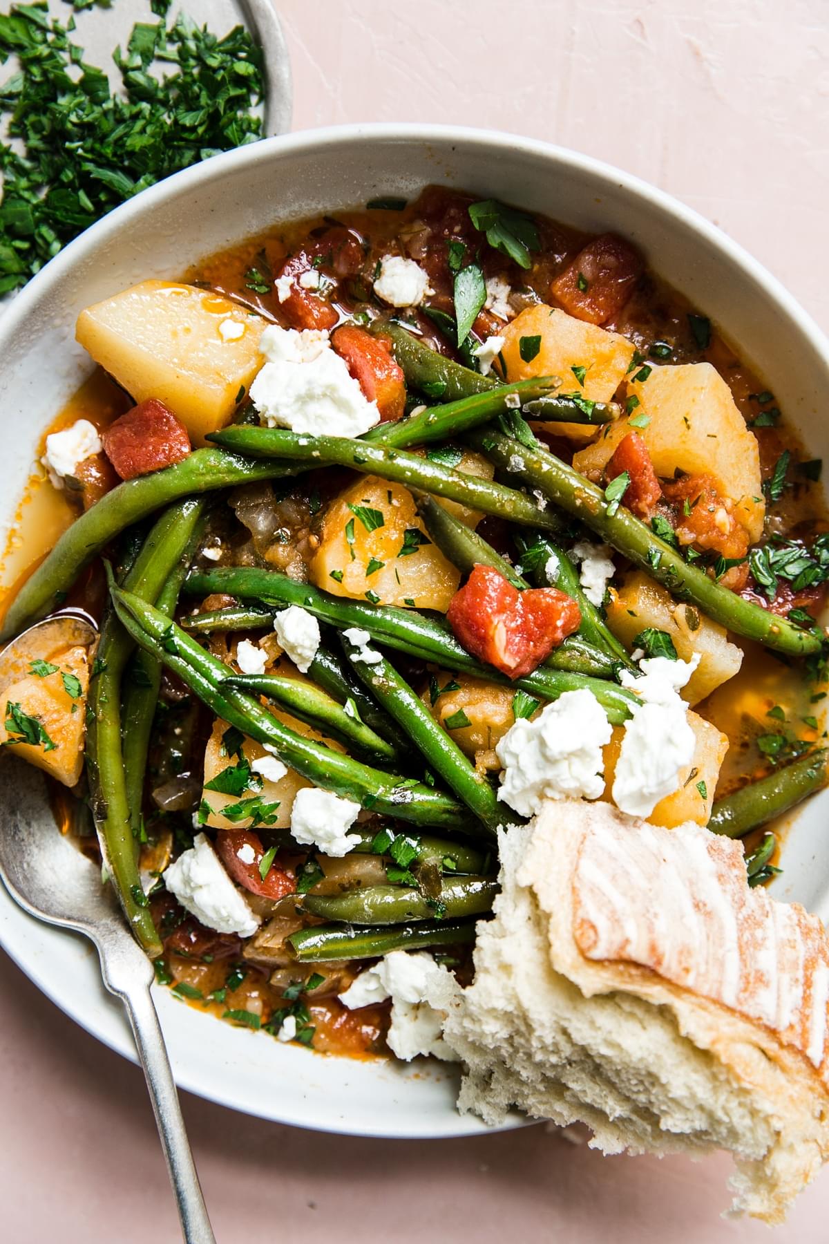 Fasolakia Greek Green Beans dish with potatoes and tomatoes in a bowl with a spoon and crusty bread