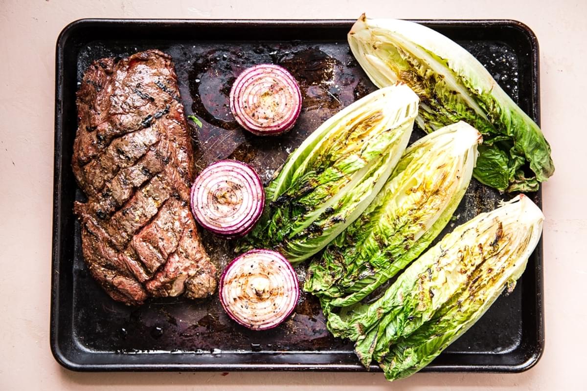 grilled skirt steak, grilled onions and grilled romaine lettuce on a baking sheet