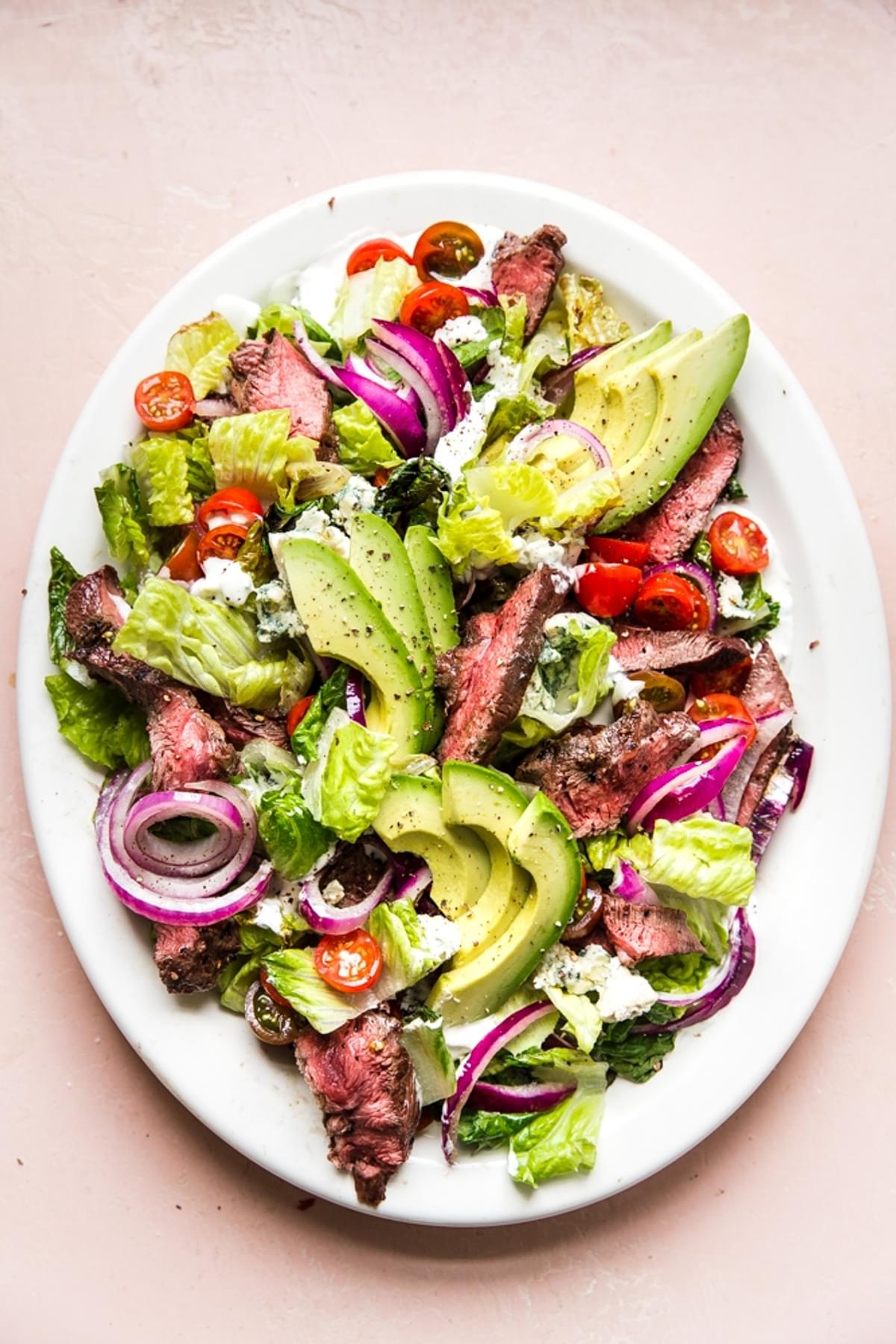 grilled steak salad with avocados, onions, tomatoes and a homemade blue cheese dressing on a large plate