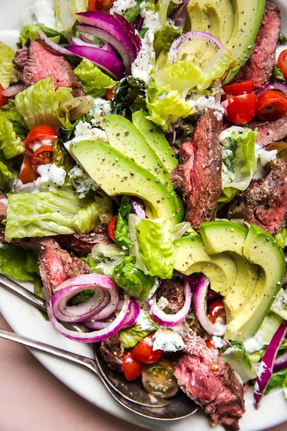 grilled steak salad with avocados, onions, tomatoes and a homemade blue cheese dressing on a large plate