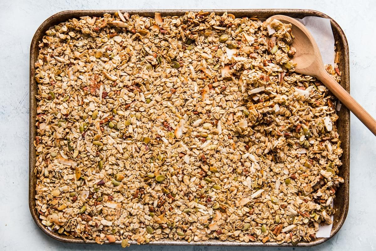 freshly baked homemade granola on a baking sheet with oats, nuts and seeds and coconut