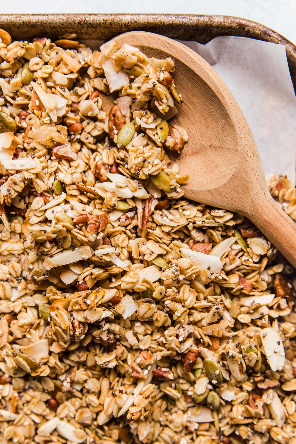 homemade granola on a baking sheet with a wooden spoon