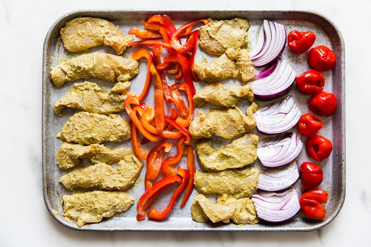Sheet pan chicken shawarma with red bell peppers and red onion on a baking sheet