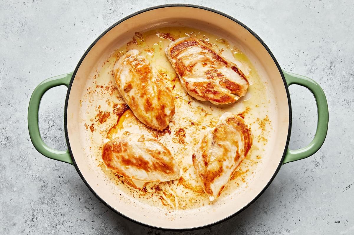 4 chicken breasts seasoned with salt being cooked in olive oil in a skillet