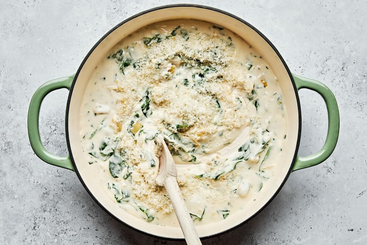 spinach and artichoke sauce being stirred with a wooden spoon with a skillet