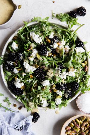 Arugula, blackberry, chèvre salad with honey mustard vinaigrette and pistachios on a plate