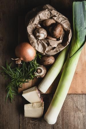 mushrooms, onions, fresh herbs, gruyere cheese and leeks on the table for homemade savory bread pudding