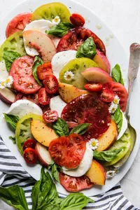 peach and tomato salad with fresh mozzarella, basil and olive oil on a large white platter.