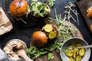 Beef sliders with sun-dried tomato mayo, arugula and sweet and spicy pickles being assembled with toothpicks.