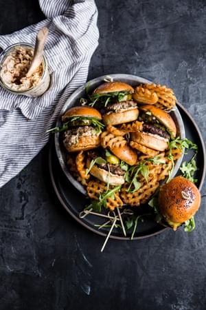 Plate of beef sliders with sun-dried tomato mayo, arugula and sweet and spicy pickles.