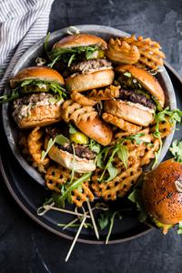 Plate of beef sliders with sun-dried tomato mayo, arugula and sweet and spicy pickles.