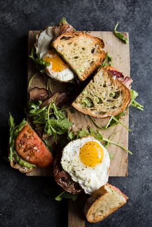 Heirloom BLT with Pesto and Fried Egg cut in half and showing the fried egg on a cutting board