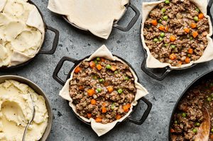 ramekins with puff pastry being filled with lamb and veggie filling to make individual shepherds pies