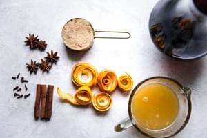 red wine, fresh orange juice, orange peels, brown sugar, star anise, cloves and cinnamon sticks in prep bowls for mulled wine