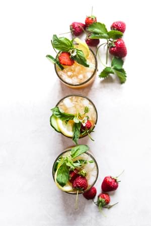 Overhead of 3 Pimm's Cup cocktails with strawberries, cucumber, lemon and basil.