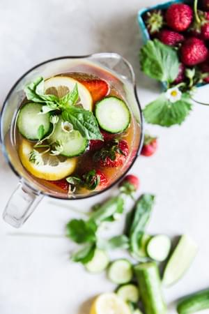 Pimm's Cup cocktail in a pitcher with strawberries, cucumber, lemon and basil.