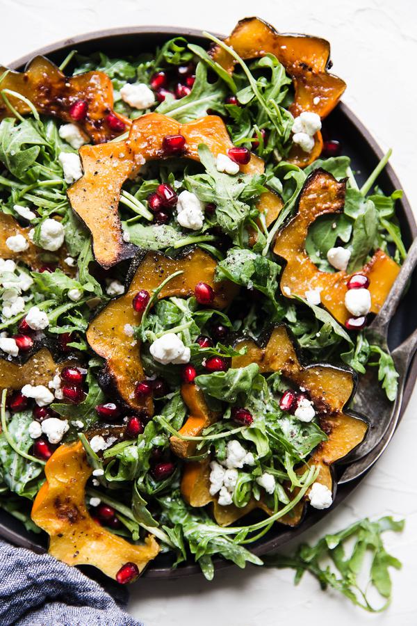 Arugula and roasted acorn squash salad with creamy goat cheese dressing pumpkin seeds and pomegranate seeds on a plate.