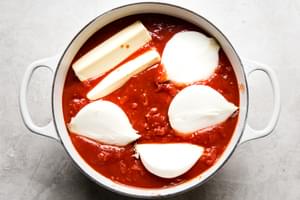 A pot filled with tomato sauce, crushed whole tomatoes, white onions and 2 sticks of butter to make homemade spaghetti sauce