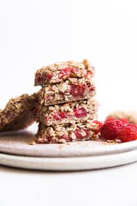 Raspberry Oatmeal Breakfast Bars stacked on a plate next to fresh raspberries.
