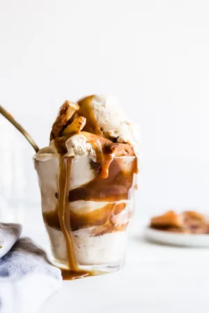 A vanilla ice cream and roasted apple sundae in a cup with a spoon and salted caramel dripping over the side.