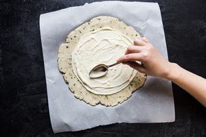 one hand using a spoon to spread crème fraîche onto pastry dough