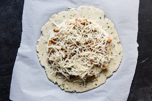 an unbaked wild mushroom galette on parchment paper with Gruyere cheese